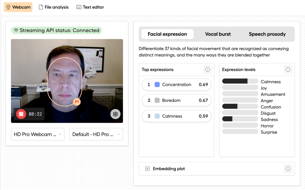 The image shows a screenshot of a software interface that appears to analyze facial expressions using a webcam feed. On the left, there is a video feed with a person's face highlighted by an orange outline, labeled "P1." The bottom section has controls for the camera and microphone settings, as well as recording functionality. On the right, there are three tabs: Facial expression, Vocal burst, and Speech prosody. The Facial expression tab is selected. It includes a description: "Differentiate 37 kinds of facial movement that are recognized as conveying distinct meanings, and the many ways they are blended together." Below, a list shows the top three detected expressions: Concentration (0.69) Boredom (0.67) Calmness (0.59) To the right, a bar chart visualizes various expression levels, including Calmness, Joy, Amusement, Anger, Confusion, Disgust, Sadness, Horror, and Surprise. Bars for "Calmness," "Confusion," and "Sadness" are more prominent compared to the others.